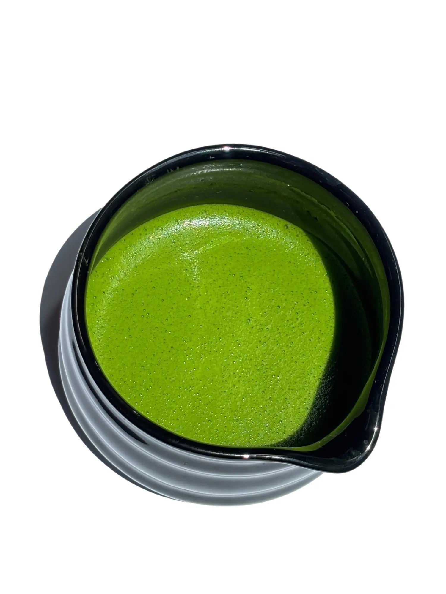 Vibrant green ceremonial matcha in a black ceramic bowl, sourced from family farms in Japan