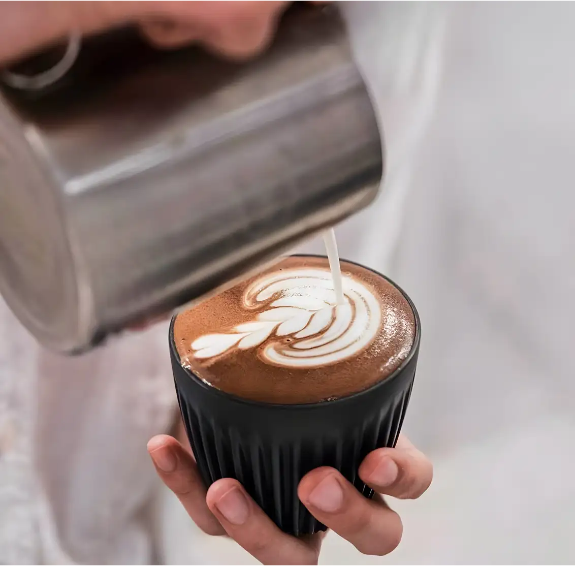 Black ribbed glass cup holding a latte with intricate white foam art.