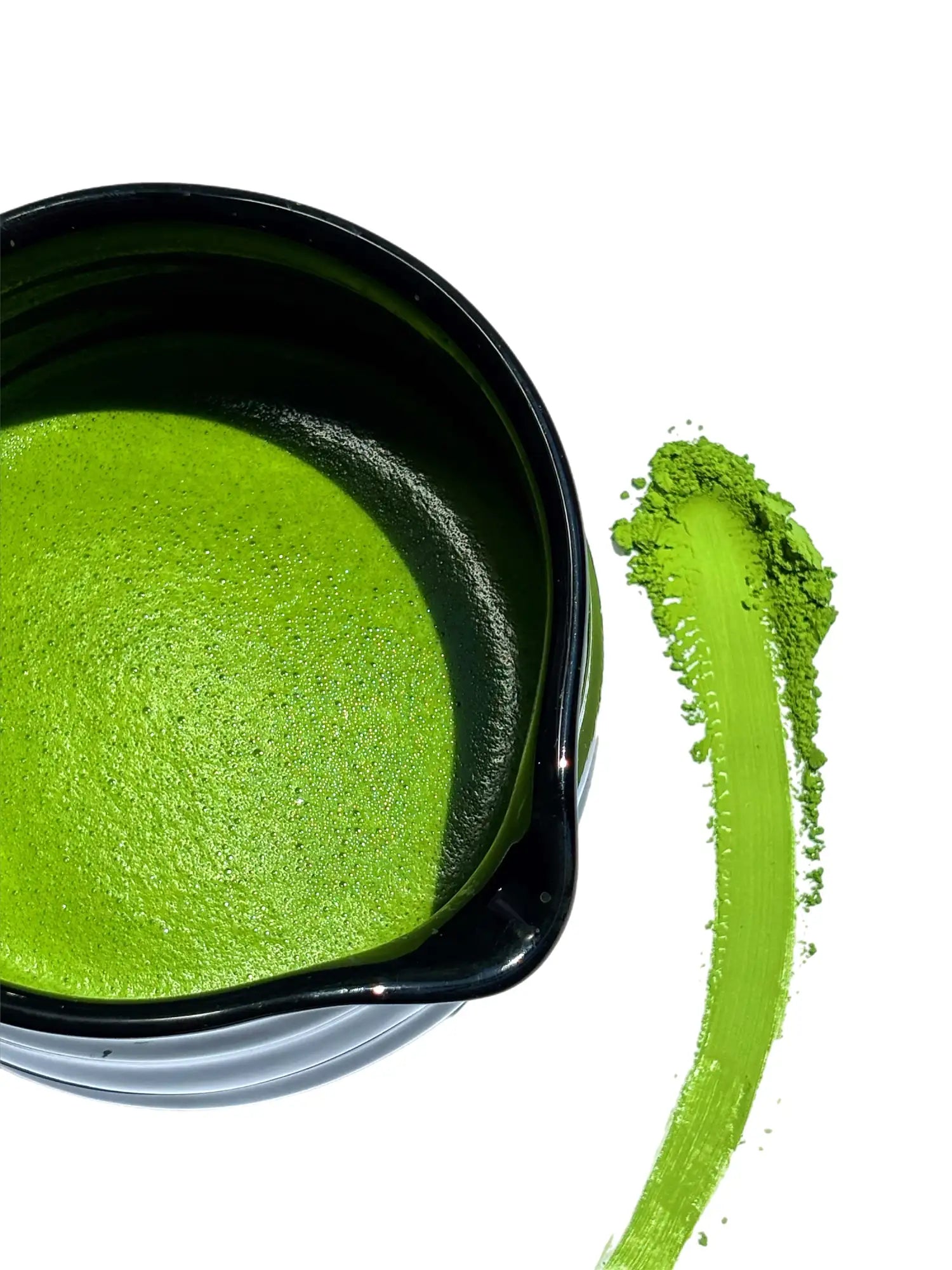 Vibrant green matcha latte in a sleek black ceramic bowl, accompanied by a streak of powdered matcha beside it.