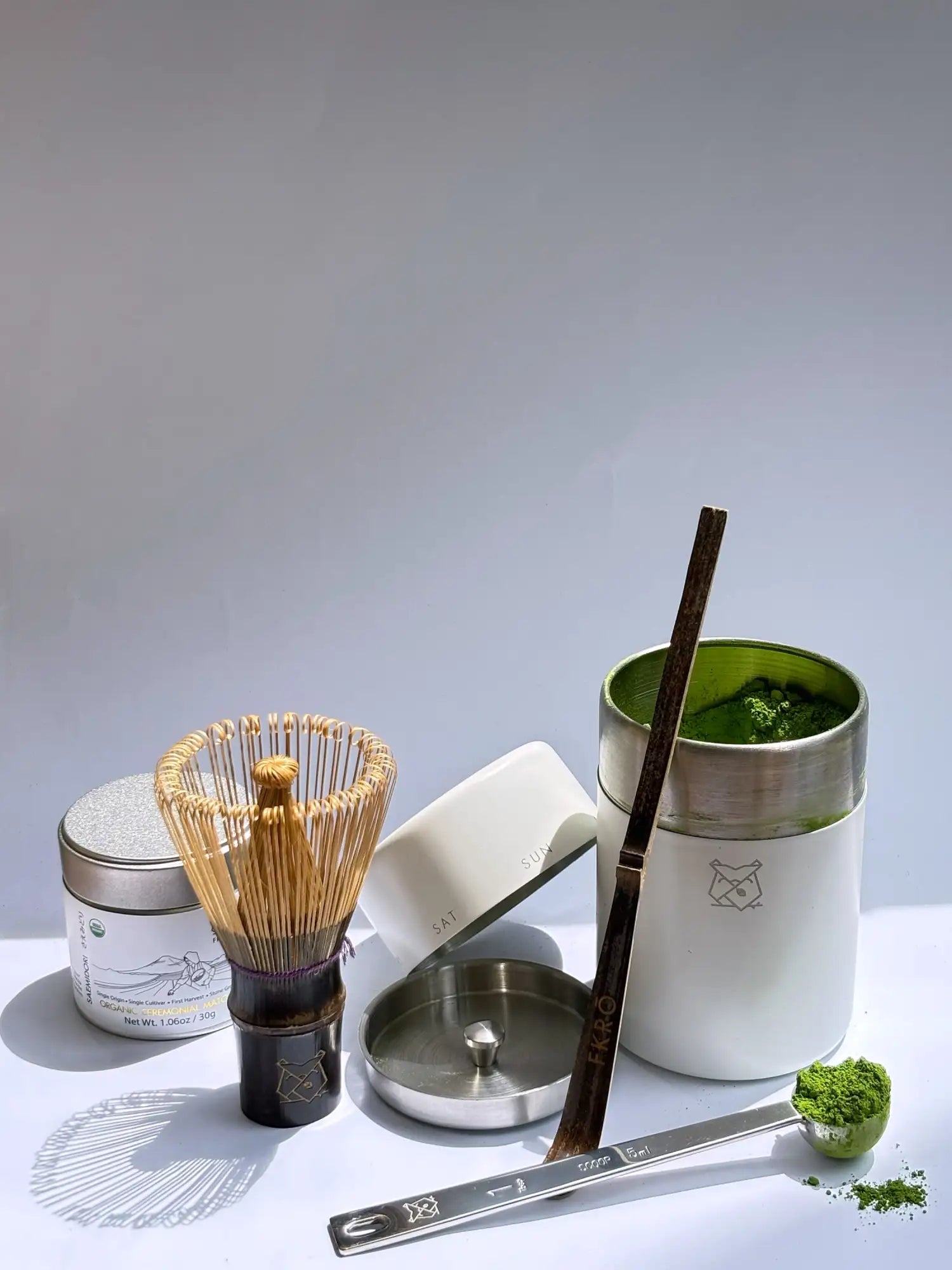 White ceramic matcha container with silver lid and green interior, holding vibrant green matcha powder
